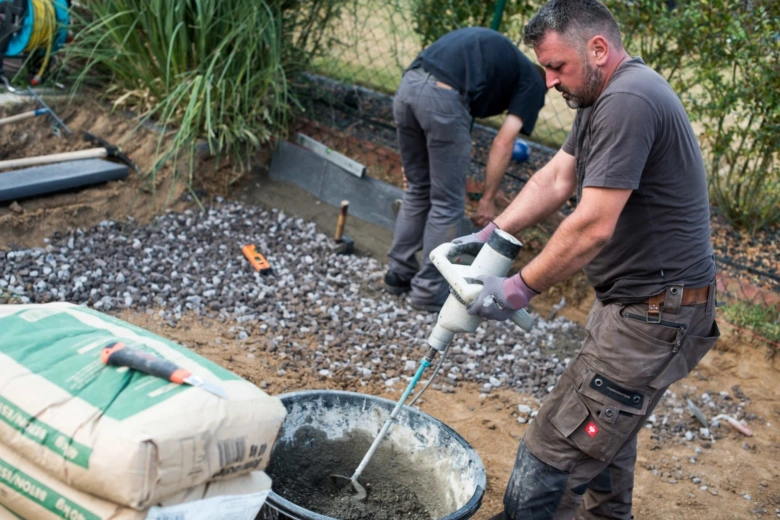 Muž míchá beton v kbelíku pomocí ručního smíchávače na staveništi.