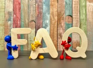 Velké dřevěné písmena FAQ s malými figurkami na pozadí.