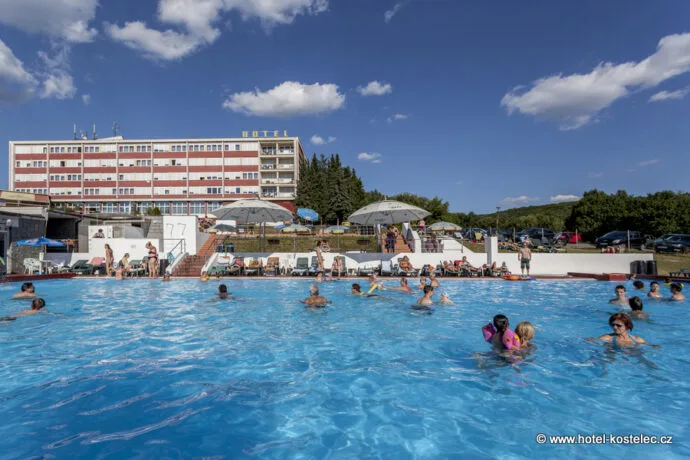 Venkovní bazén s lidmi v Otrokovicích před hotelovou budovou.