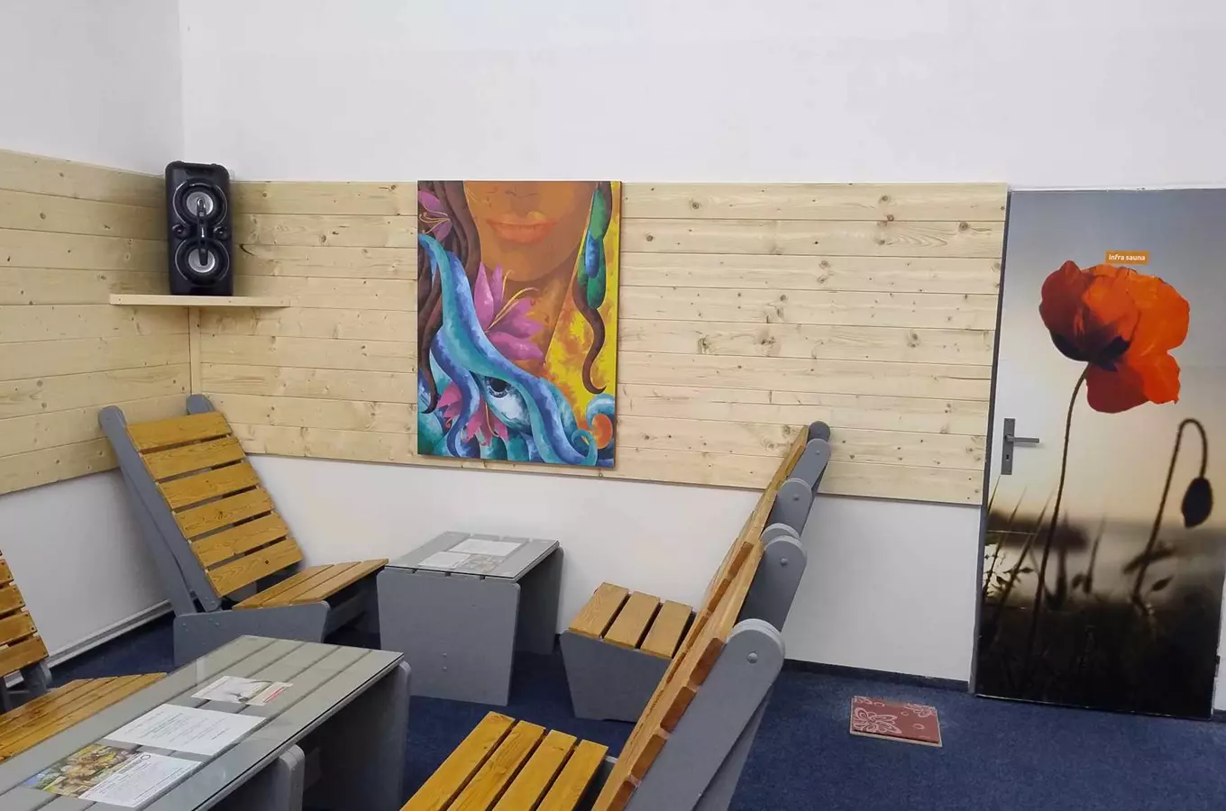 Vnitřek sauny s dřevěnými židlemi a barevnou malbou na stěně.