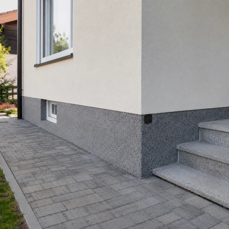Modern dům s omítkou na horní části a šedým obkladem dole.