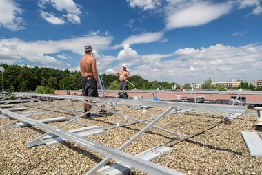 Dva dělníci montují rámy pro fotovoltaickou elektrárnu na střechu.