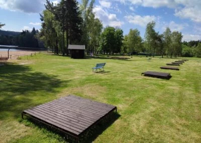Dřevěné lehátka na trávníku v okolí koupaliště.