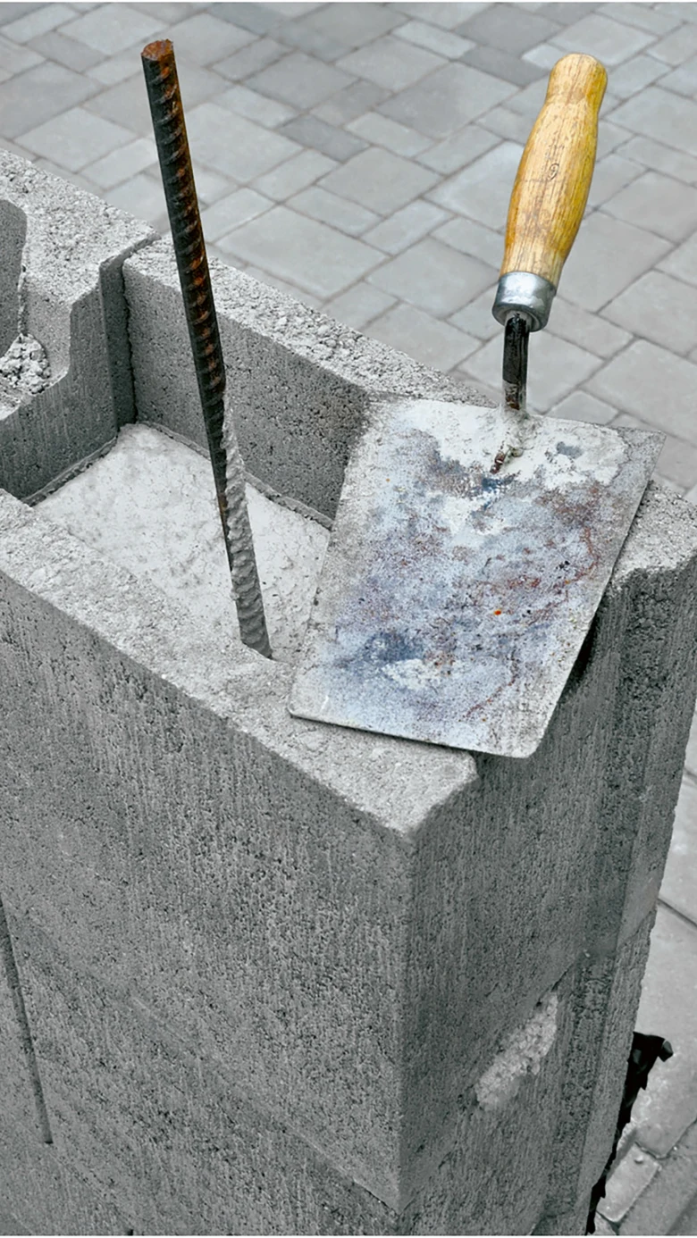 Kladivo na maltu a ocelová tyč vedle betonového bloku.