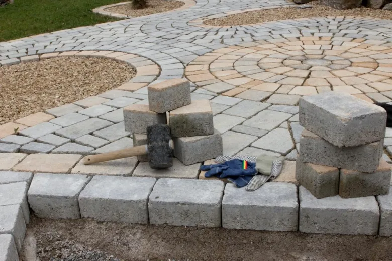 Sedí betonová dlažba s kladivem rukavicemi na zahradě.
