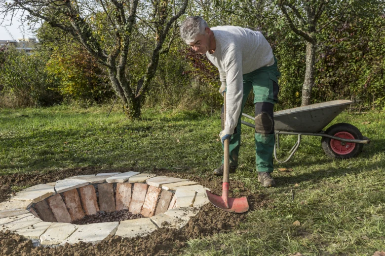 Muž staví ohniště z cihel ručně v zahradě.