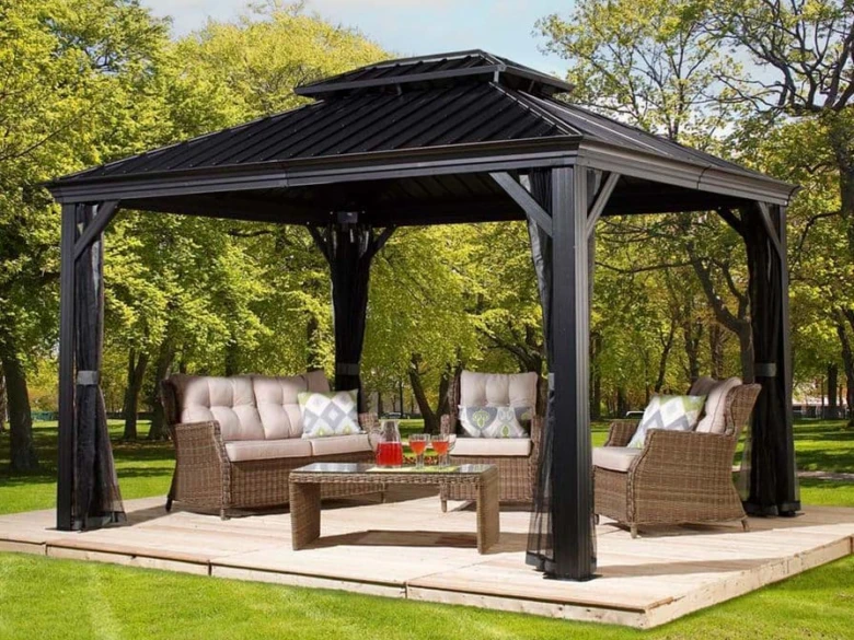 Černá zahradní pergola s pohovkou na dřevěné terase uprostřed zelené zahrady.