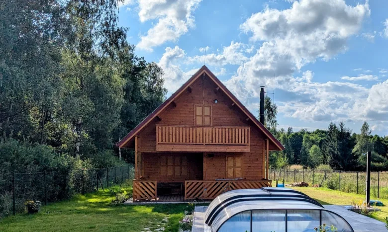 Dvoupatrová dřevěná chata s balkony na zelené louce pod modrou oblohou.