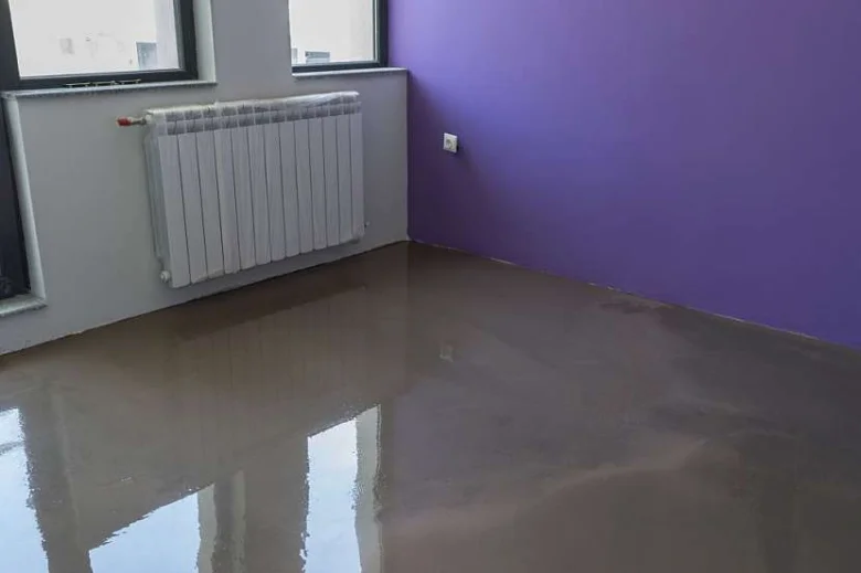 Nově nanesená hladká nivelační stěrka v interiéru s reflektující podlahou.