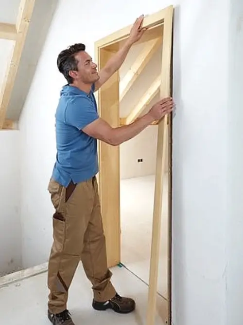 Muž montuje dřevěný zárubní pro vnitřní dveře.