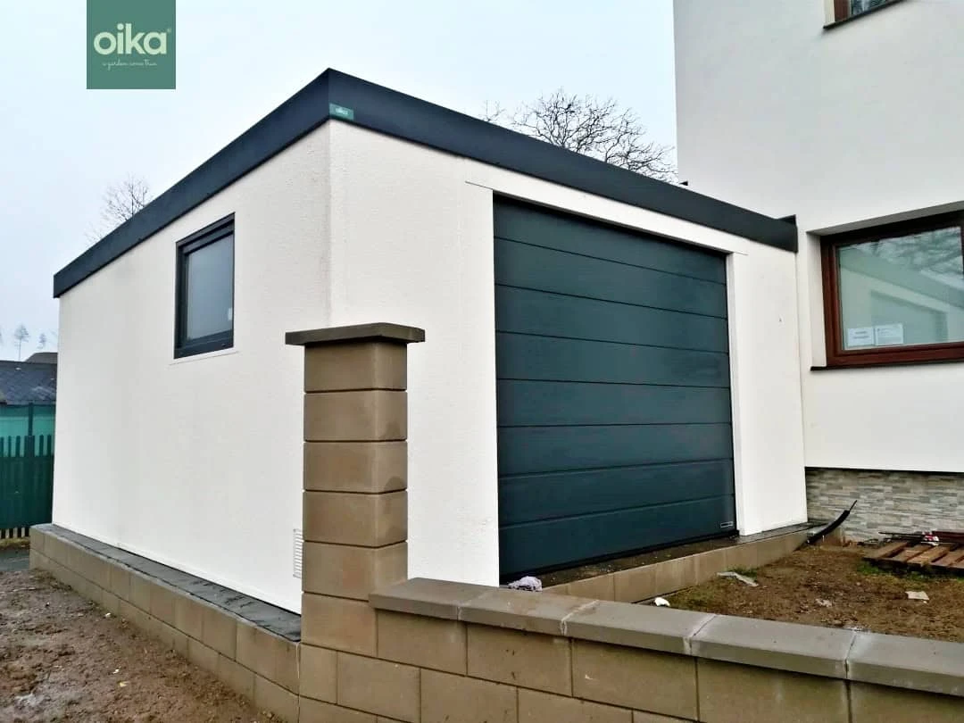 Modernizovaná garáž s bílou fasádou a tmavě zelenými dveřmi.