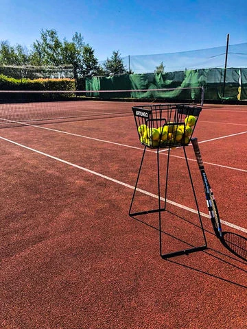 Korb s tenisovými míčky na červeném dvorci v Hracholuskách.