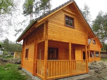 Nově postavená dřevěná chata s terasou uprostřed lesa.