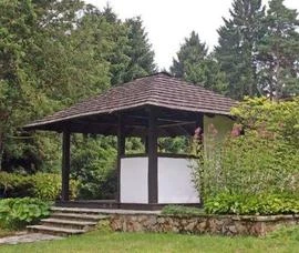 Pavilón s doškovou střechou uprostřed zelené přírody.
