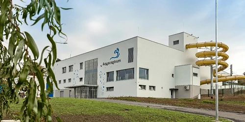 Bílá budova Aquacentrum s žlutou vodní skluzavkou venku.
