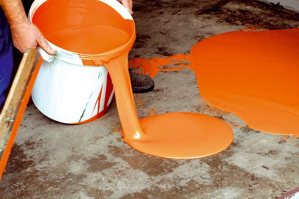 Nalévání oranžové epoxidové stěrky na betonovou podlahu.