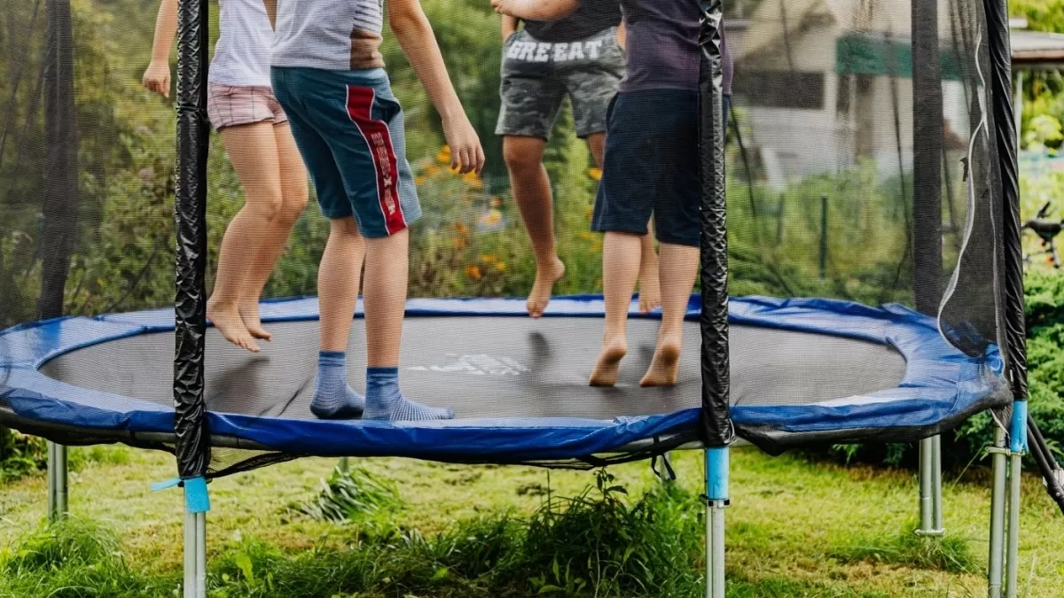 Děti skáčou na trampolíně v zahradě.