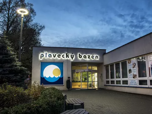 Vstup do plaveckého bazénu s osvětleným nápisem v noci.