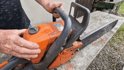 Oranžová motorová pila s řetězem na dřevěné lavice.