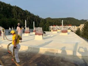 Pracovníci nanášejí bílou izolační pěnu na střechu.