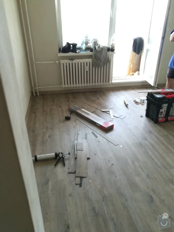 Instalace vinylové podlahy s rozloženými deskami a nářadím.