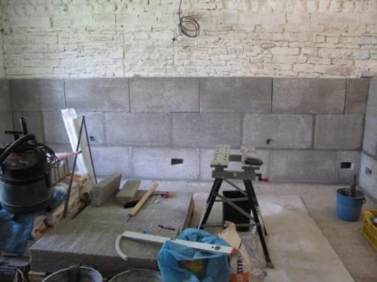 Práce na soklu domu s cihlovou zdí nahoře a betonovými bloky dole.