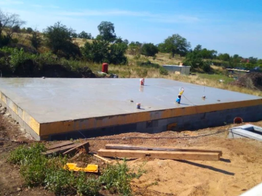 Stavební místo s čerstvě nalitým kartáčovaným betonem na základové desce.